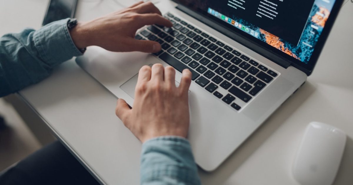 Mãos a digitar num portátil com gráficos de website e ícones de domínio e hosting, simbolizando a gestão integrada de um negócio online.